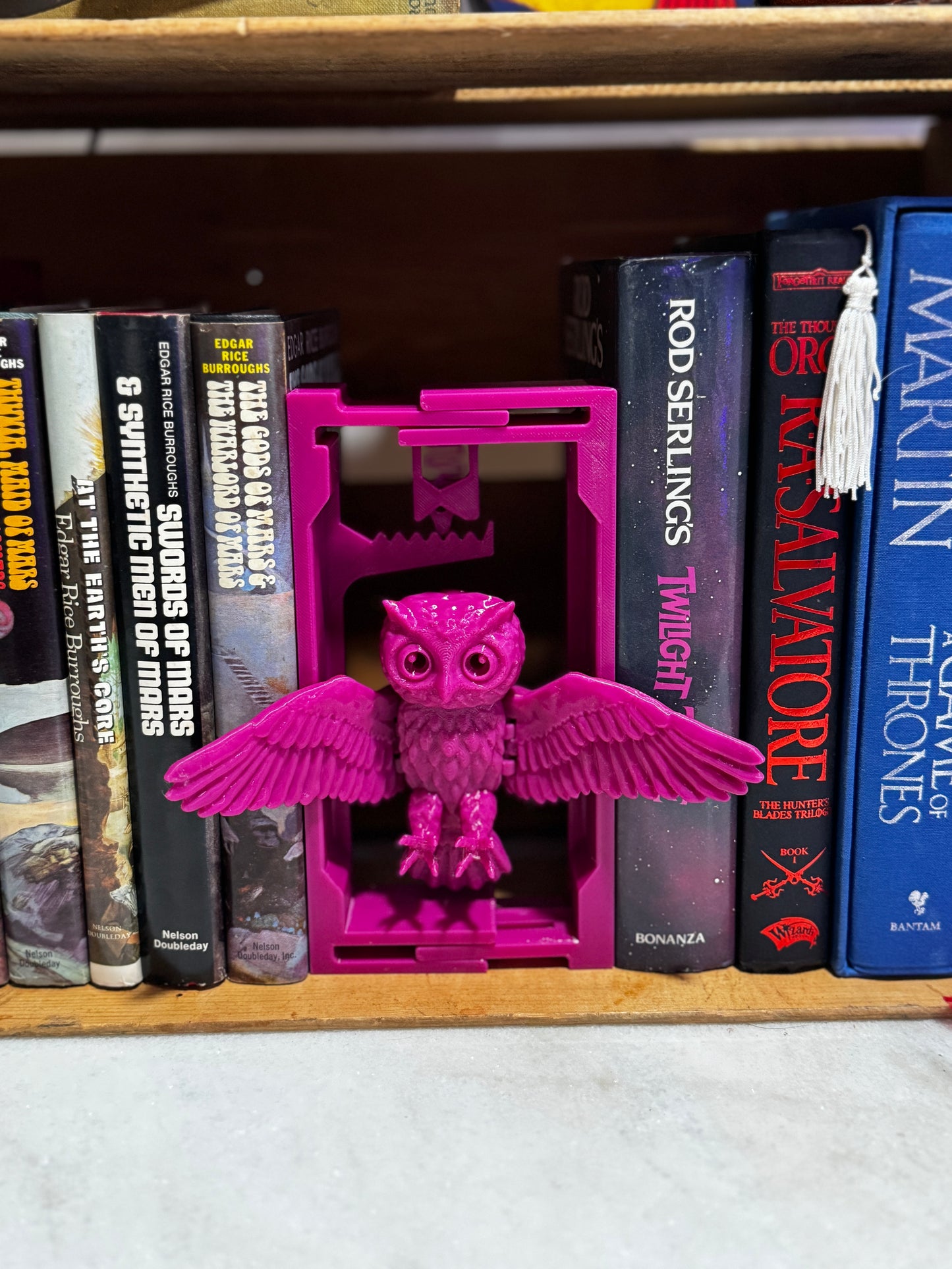 3D-printed adjustable owl book nook filling a gap on a wooden bookshelf.